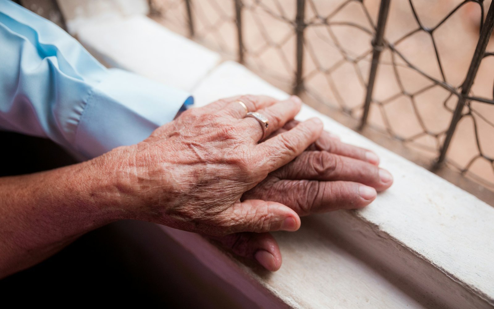Close-up of an elderly person's clasped, wrinkled hands resting on a windowsill, representing elder care and guardianship for ageing parents in Colombia